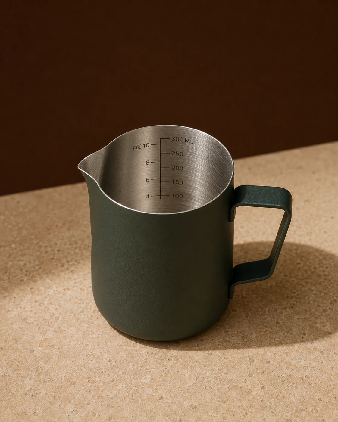 Precision Milk Pitcher in Dark Green — travertine surface, engraved ml and oz measurement markings visible