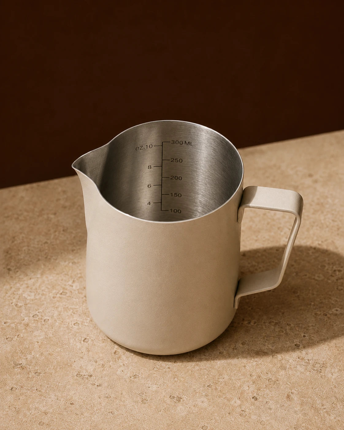 Precision Milk Pitcher in Beige — travertine surface, engraved ml and oz measurement markings visible