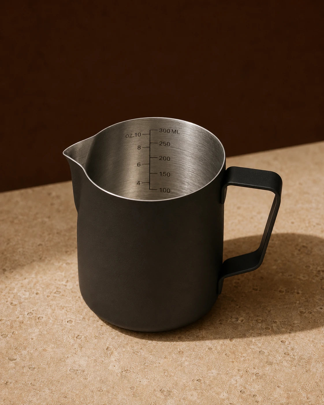 Precision Milk Pitcher in Black — travertine surface, engraved ml and oz measurement markings visible