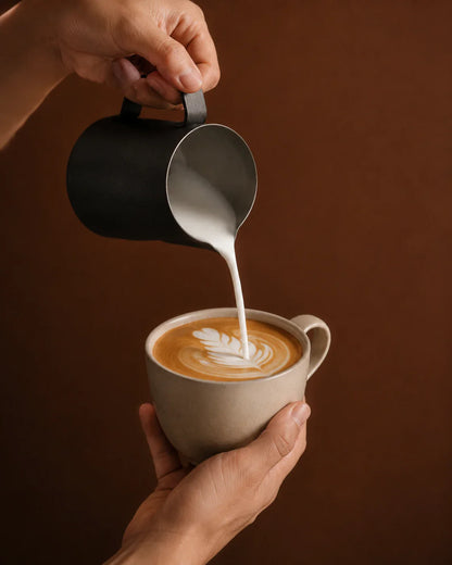 Precision Milk Pitcher — steamed milk being poured into latte art, warm brown background