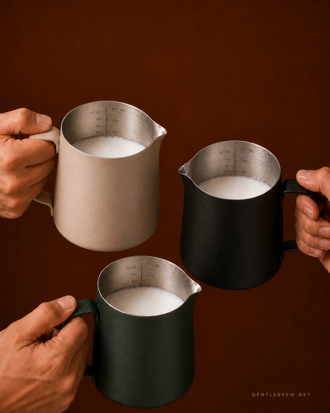 Precision Milk Pitcher — Black, Beige and Dark Green held with steamed milk, all three finishes